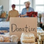 Volunteers sort clothes and food in a donation center. Cardboard sign reads 'Donation.'